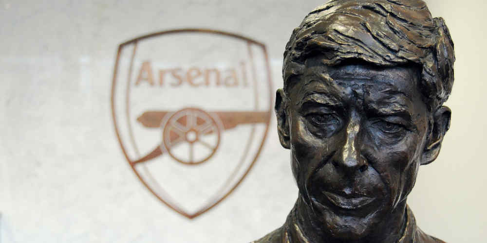 Arsène Wenger statue with Arsenal logo in the background
